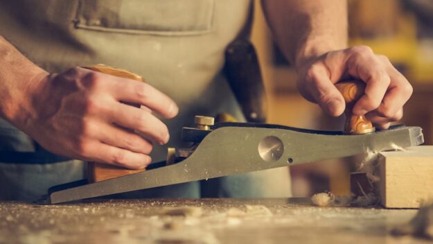 Vakman uit de regio die met een schaafmachine een houten oppervlak bewerkt in zijn werkplaats.